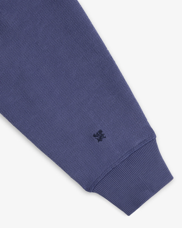 A close-up of the Stone Washed Marina Hoodie’s blue textured sleeve, ribbed cuff, and stitched dark blue wrist logo.