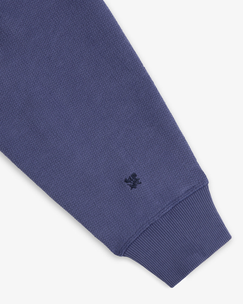A close-up of the Stone Washed Marina Hoodie’s blue textured sleeve, ribbed cuff, and stitched dark blue wrist logo.