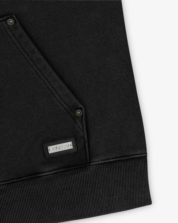 Close-up of a black Washed Full Zip Hoodie pocket with metal rivets and a branded rectangular metal plate.