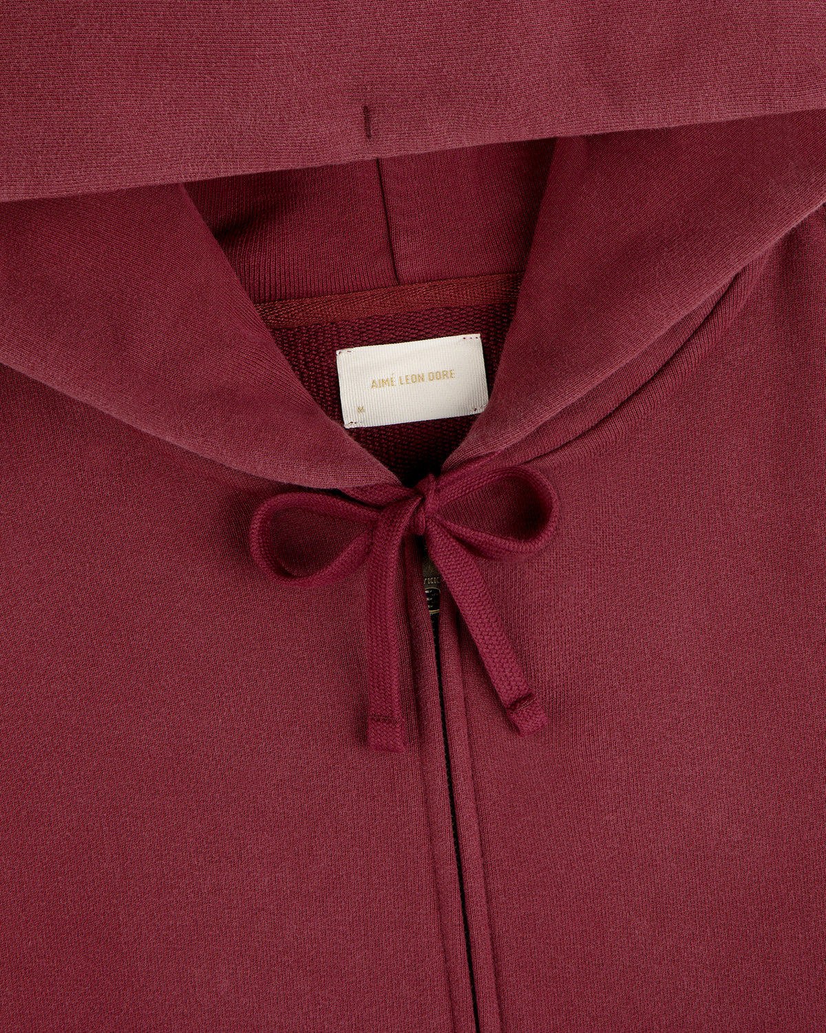Close-up of a dark red Washed Full Zip Hoodie with drawstrings and a brand label at the neckline.
