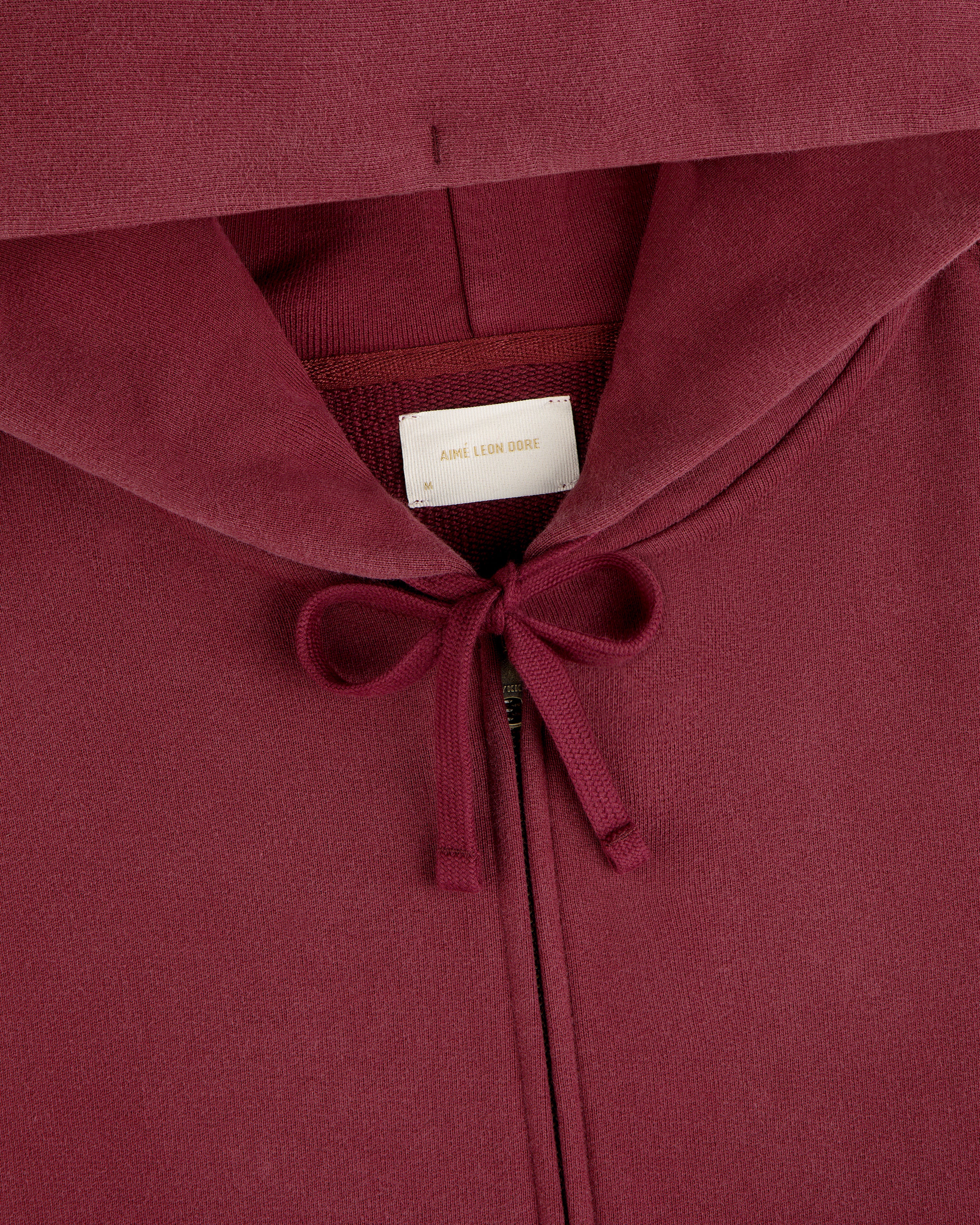 Close-up of a dark red Washed Full Zip Hoodie with drawstrings and a brand label at the neckline.