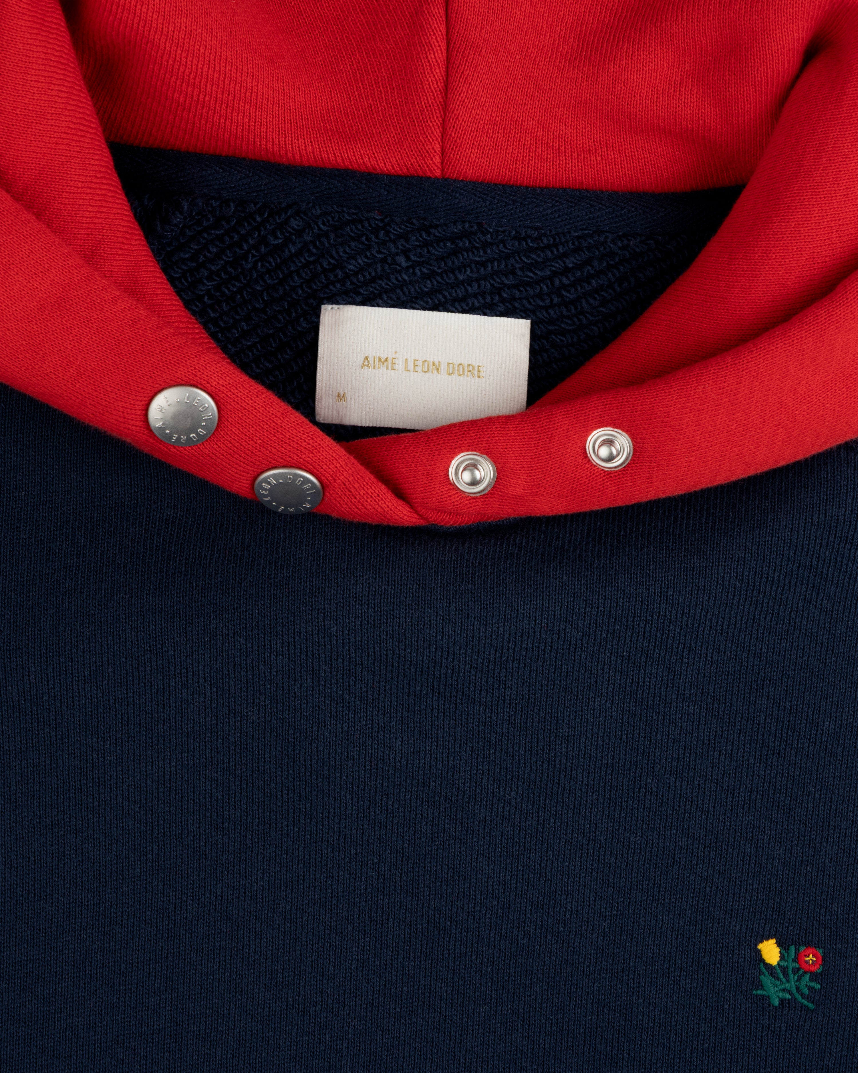 Colorblock Crest Snap Hoodie: navy hoodie with a red hood, snap-button collar, and small floral embroidery near the hem.