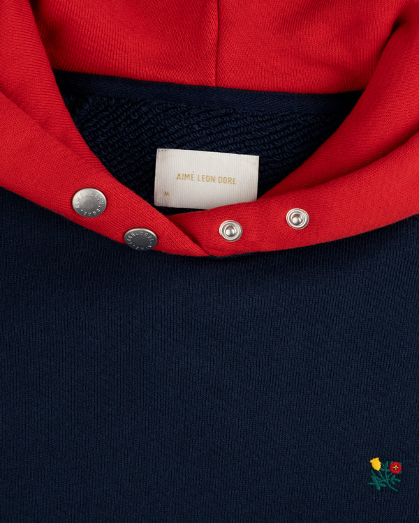 Colorblock Crest Snap Hoodie: navy hoodie with a red hood, snap-button collar, and small floral embroidery near the hem.
