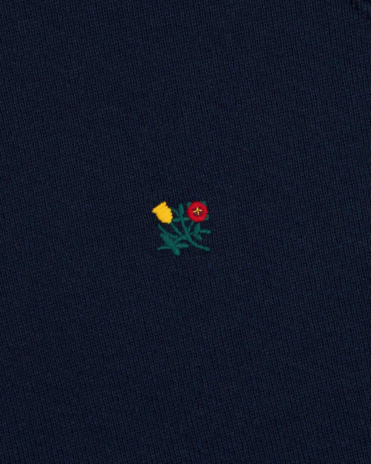 Small embroidered yellow and red flower design on the dark blue knit fabric of a Colorblock Crest Snap Hoodie.