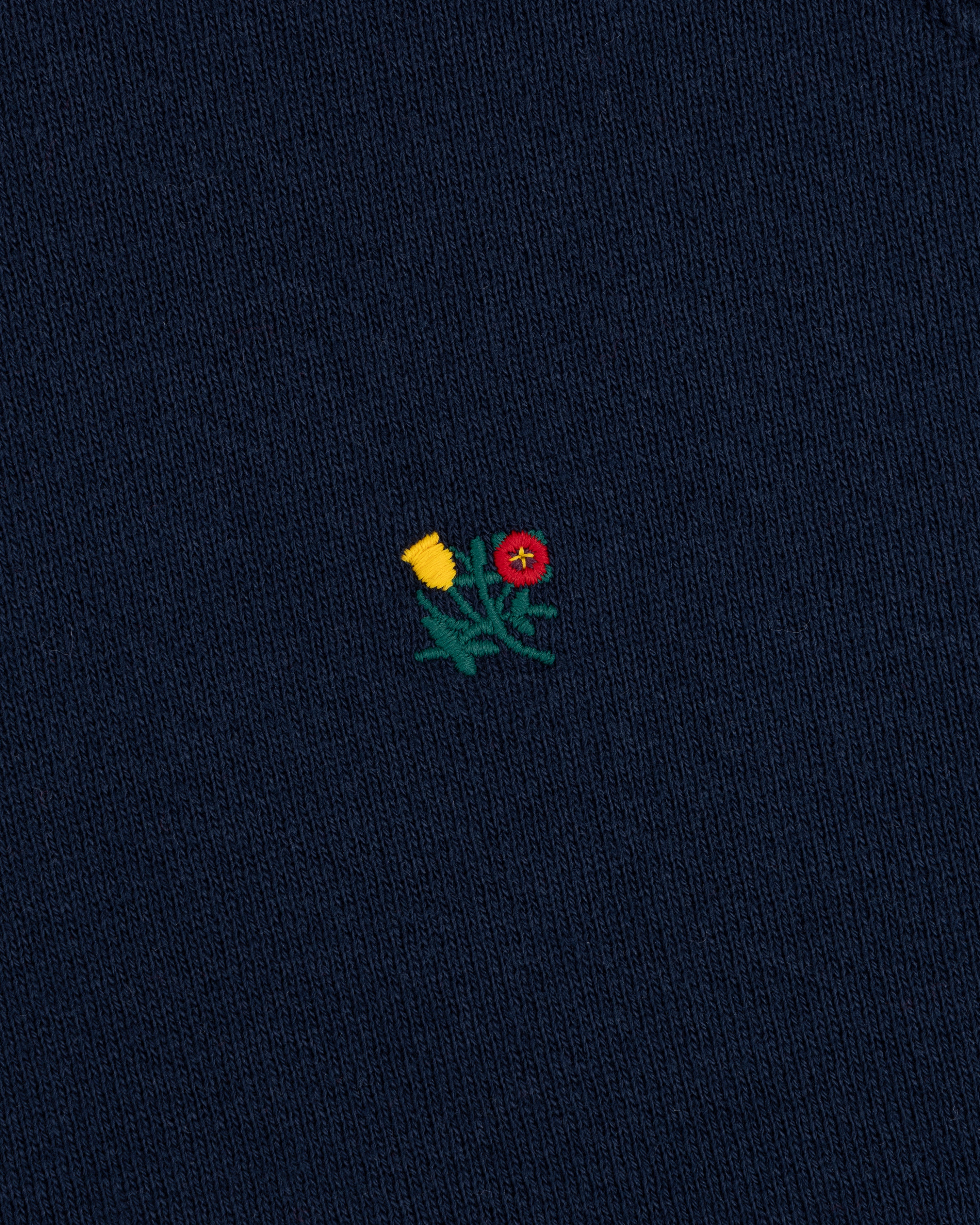Small embroidered yellow and red flower design on the dark blue knit fabric of a Colorblock Crest Snap Hoodie.