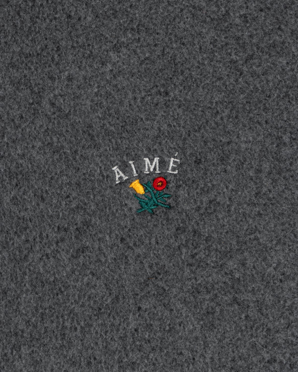 Gray textured fabric with Crest logo and AIMÉ embroidered above a small flower on the front center of the hoodie.