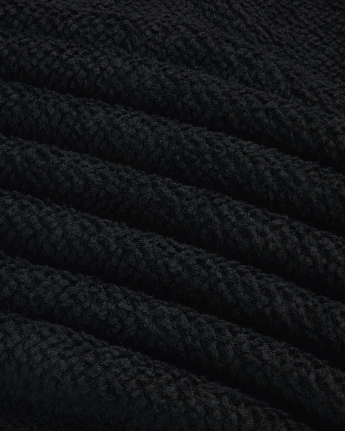 Close-up of black textured fleece fabric from a Fleece Performance Hoodie, showing diagonal folds.