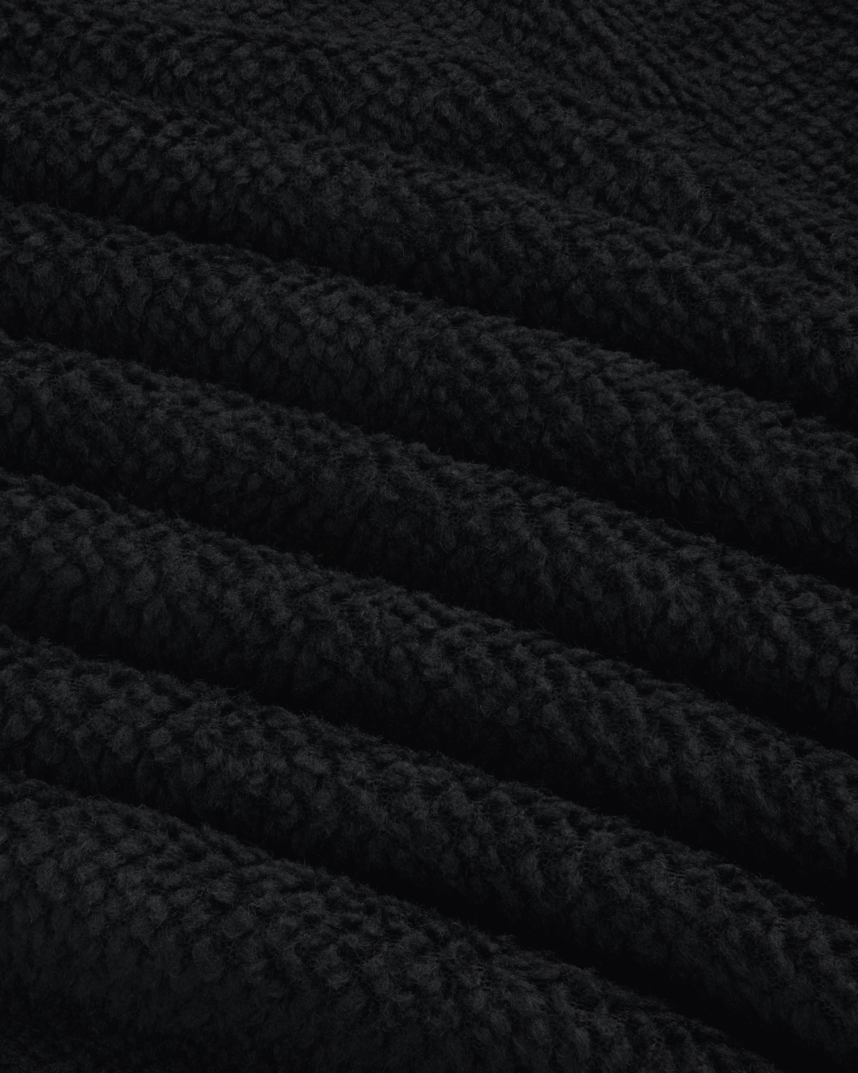 Close-up of black textured fleece fabric from a Fleece Performance Hoodie, showing diagonal folds.