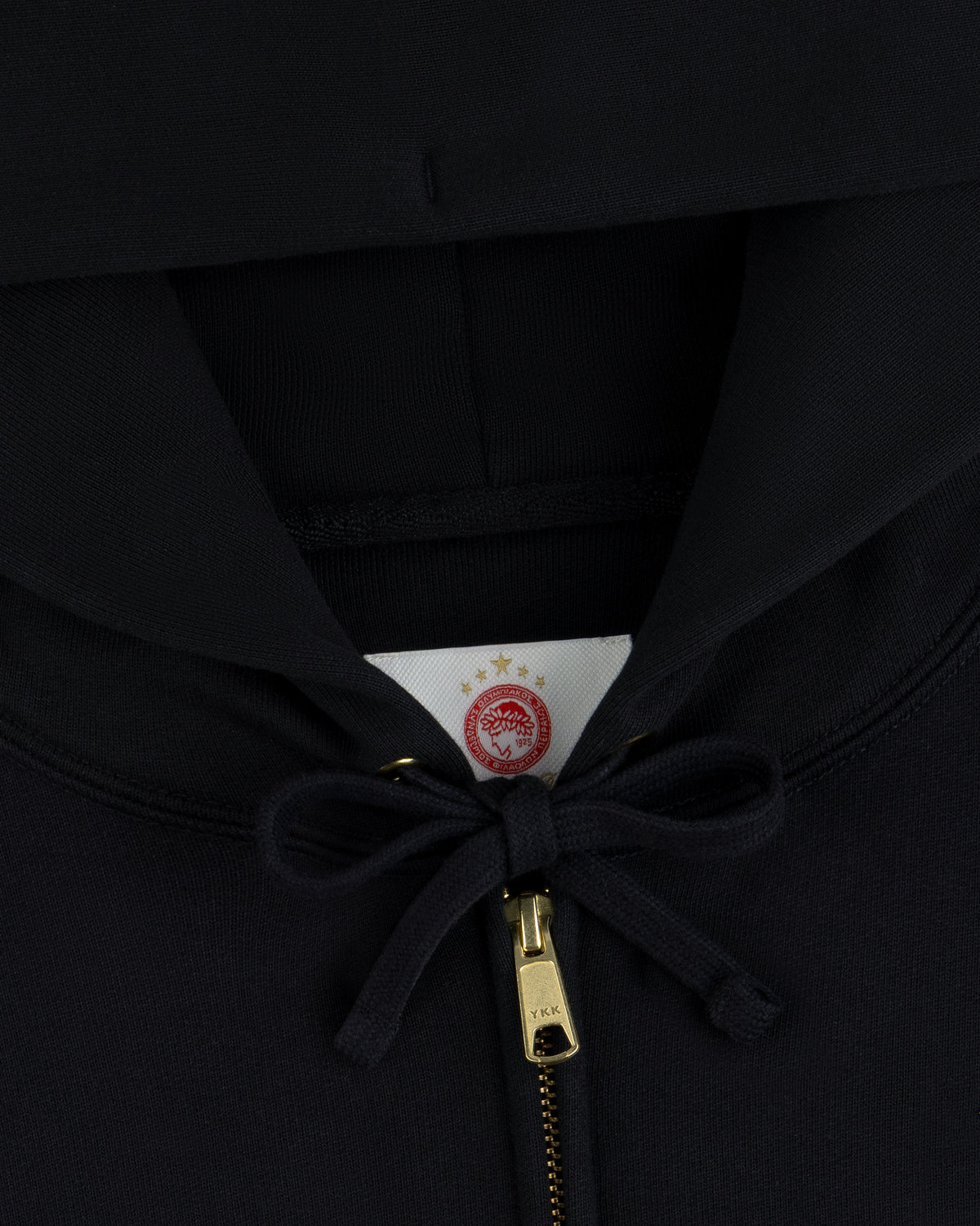ALD / Olympiacos F.C. Full Zip Hoodie in black with a gold zipper and a circular team logo on the interior neck label.