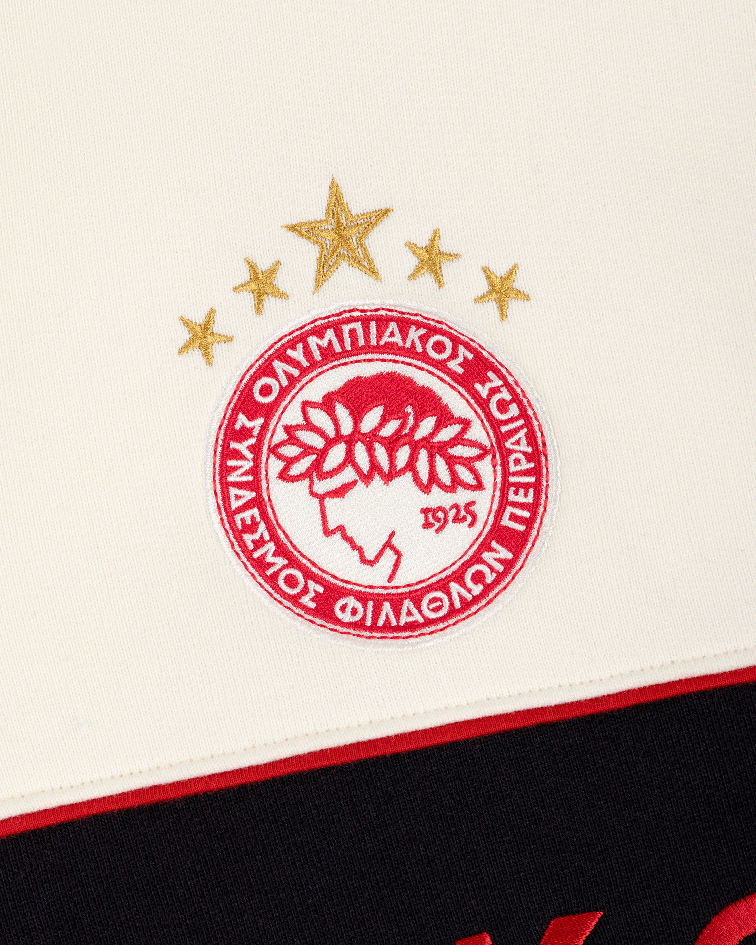 ALD / Olympiacos F.C. Full Zip Hoodie with an embroidered red and white club crest and three gold stars on a cream hoodie.