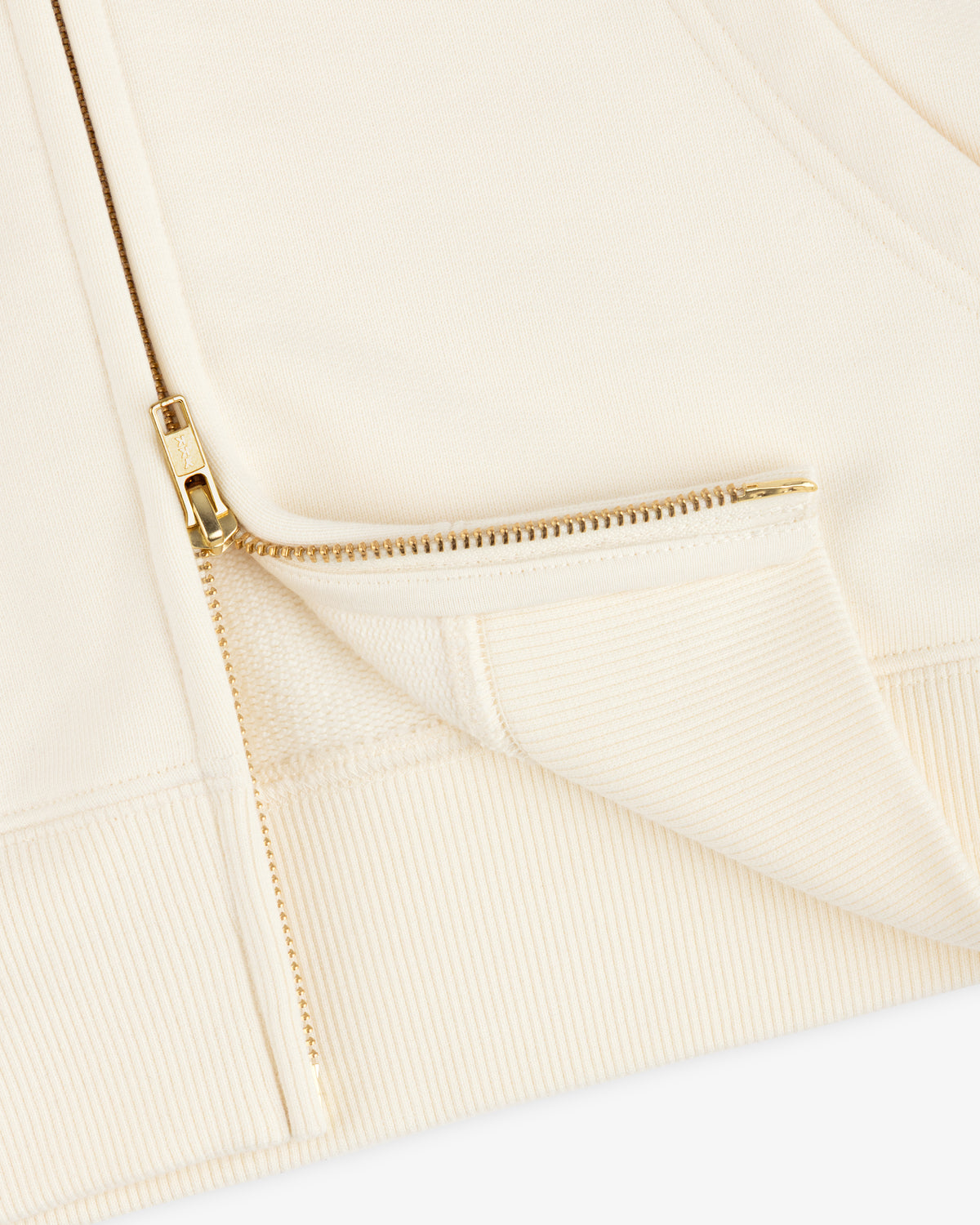 Close-up of a cream-colored ALD / Olympiacos F.C. Full Zip Hoodie with a gold-toned metal zipper.