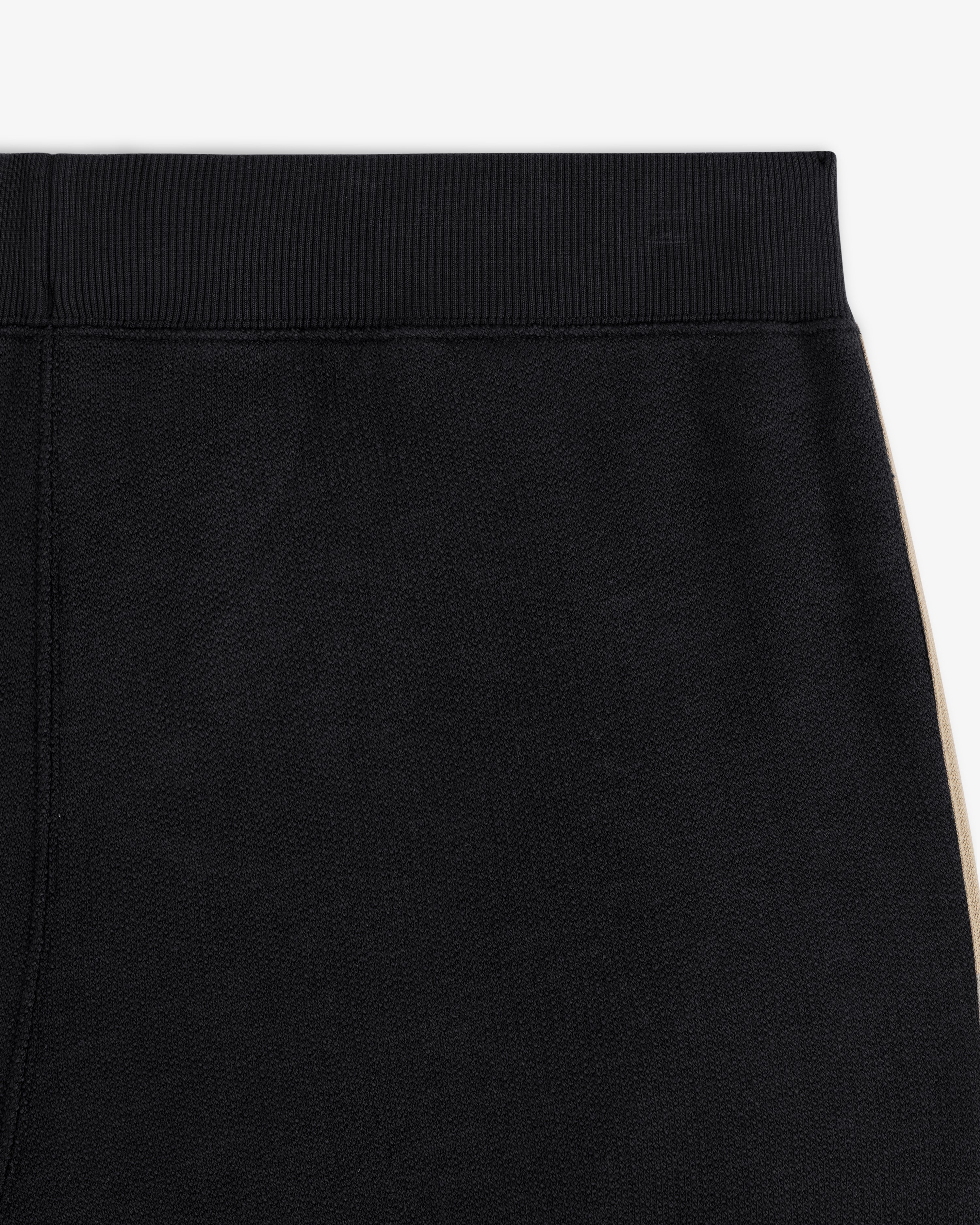 Close-up of Saint George Track Pant—black with a ribbed waistband and beige side stripe.