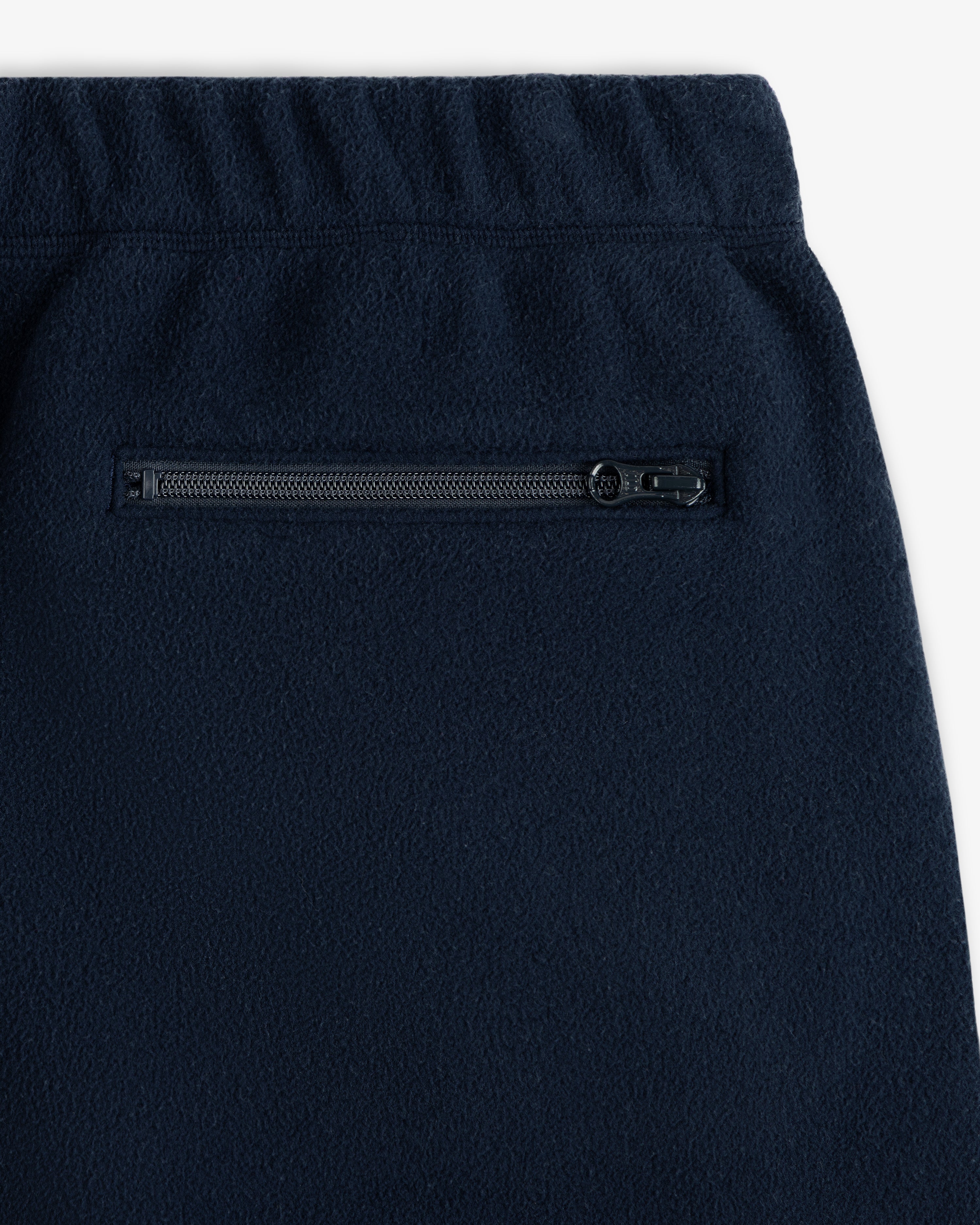 Close-up of the Crest Fleece Sweatpant in navy blue, featuring an elastic waistband and a zippered pocket.