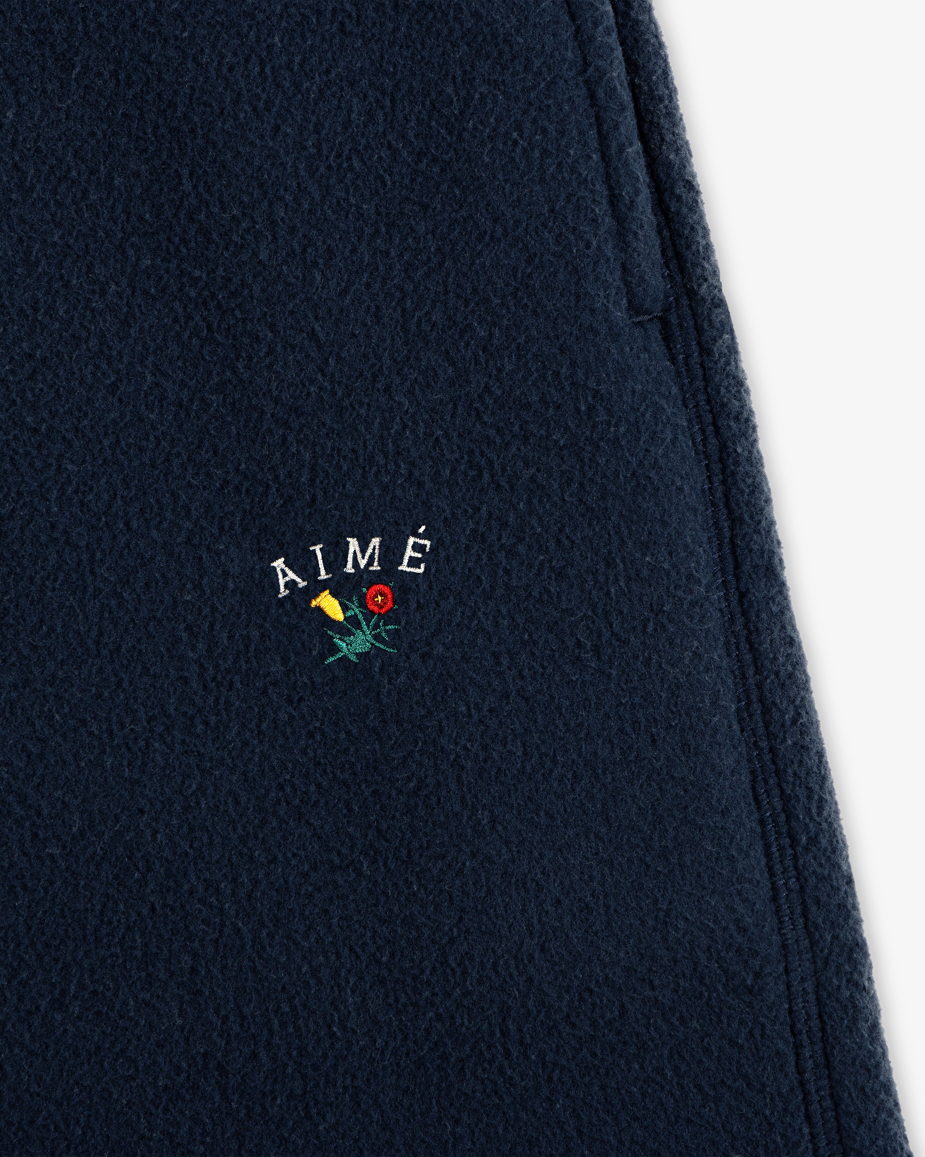 Crest Fleece Sweatpant in navy with AIMÉ and yellow/red flower embroidery above the zipper pocket.