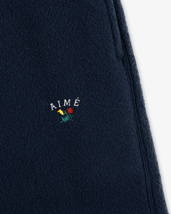 Crest Fleece Sweatpant in navy with AIMÉ and yellow/red flower embroidery above the zipper pocket.