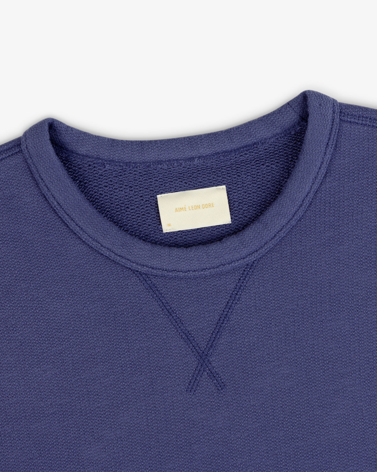 Close-up of Stone Washed Marina Crewneck Sweatshirt with visible stitching and beige Aime Leon Dore collar label.