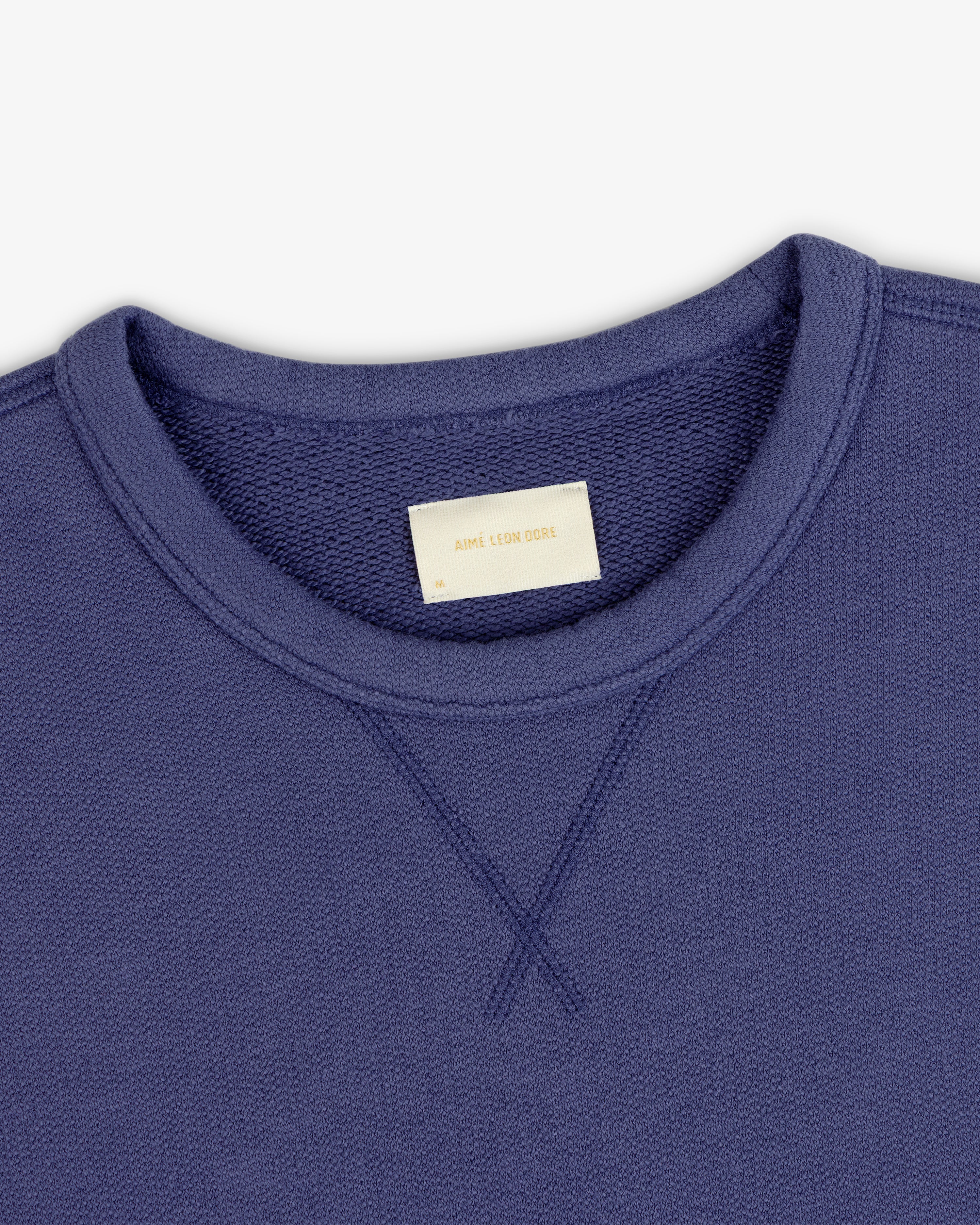 Close-up of Stone Washed Marina Crewneck Sweatshirt with visible stitching and beige Aime Leon Dore collar label.