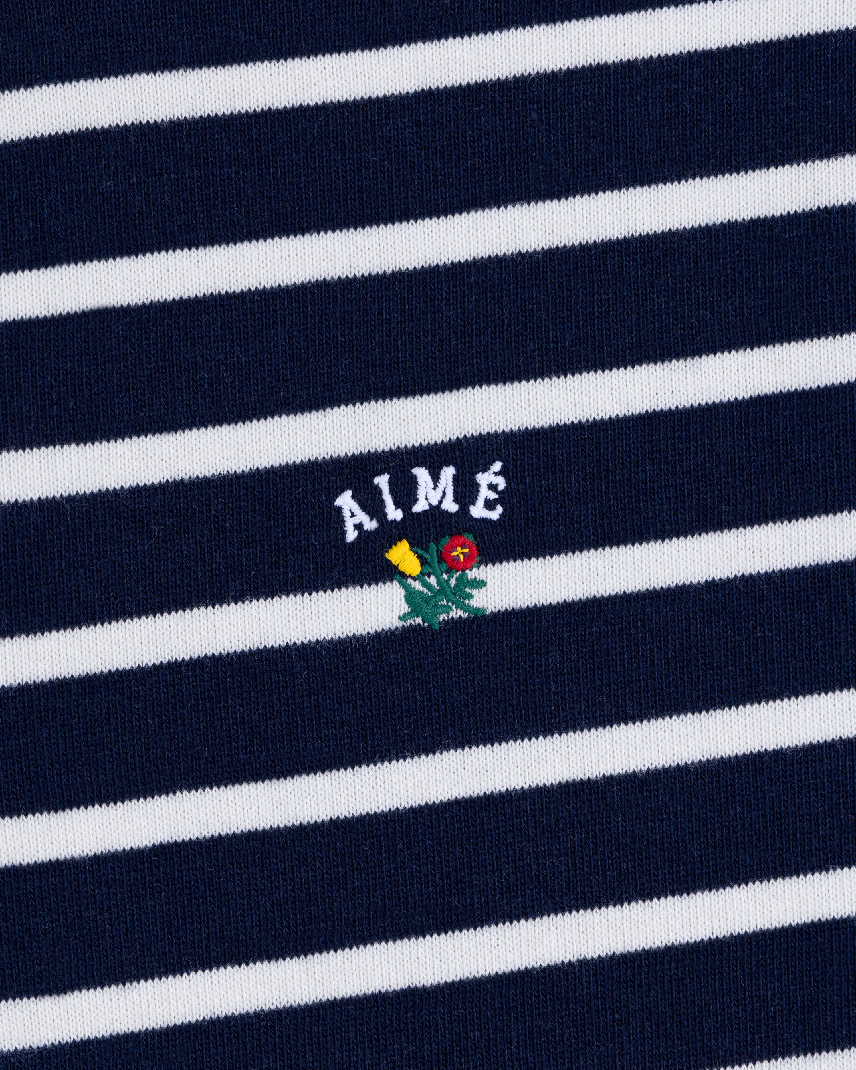 Striped Crest Quarter Zip in navy and white with AIMÉ text and a small embroidered yellow and red flower beneath.