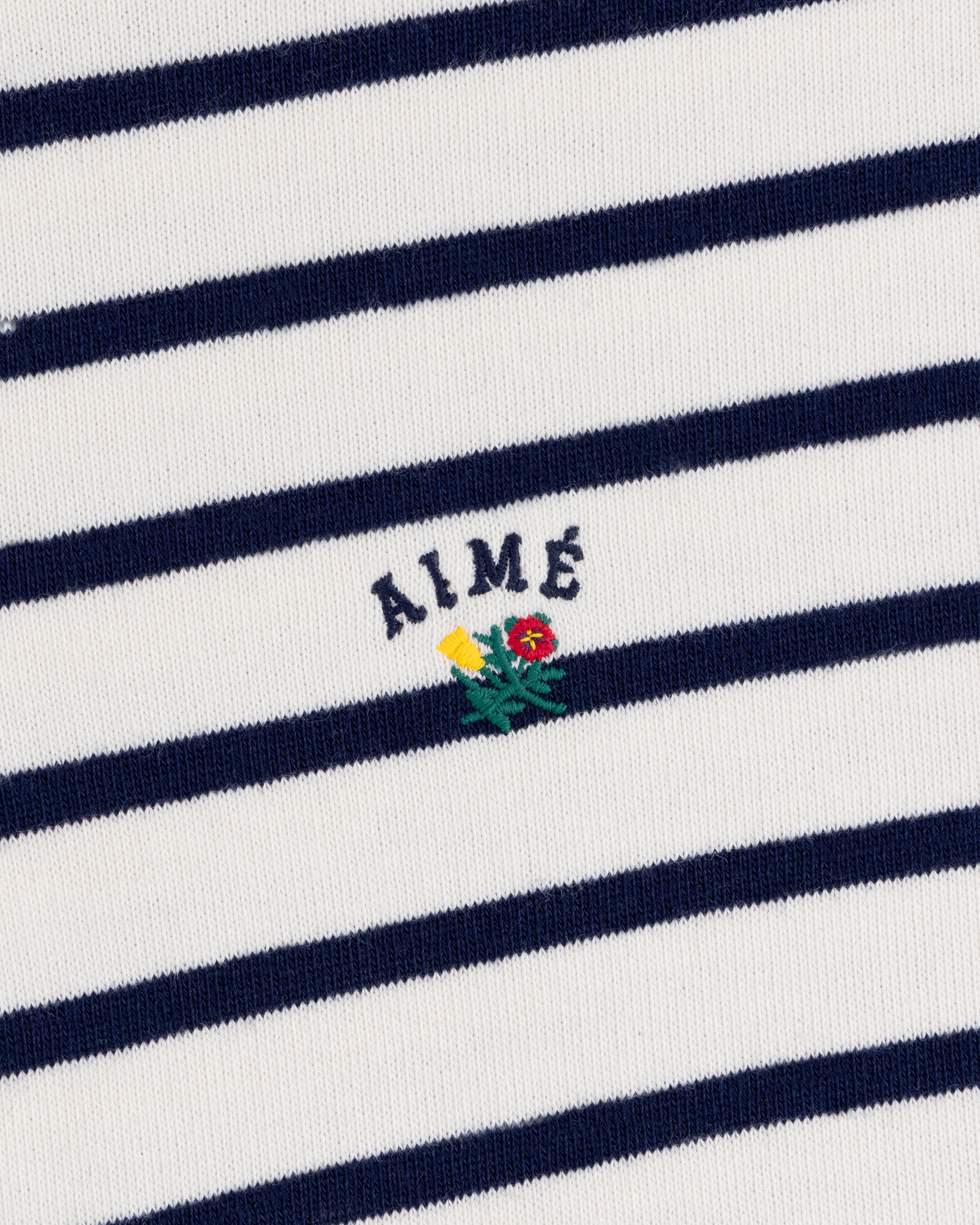 Striped Crest Quarter Zip: White with navy stripes, AIMÉ text, and small yellow/red embroidered flowers below.