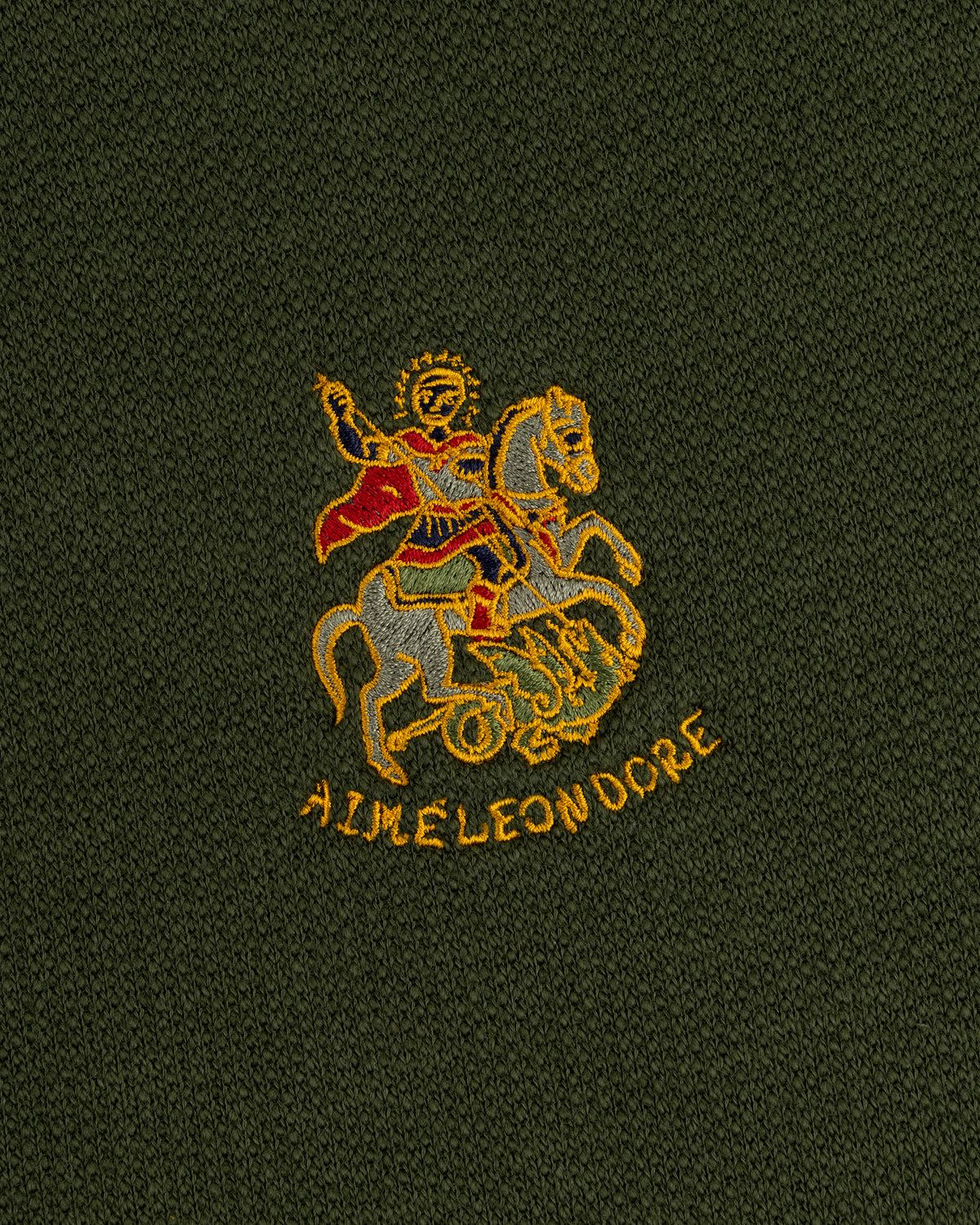 Saint George Track Jacket: Embroidered rider in red cape over yellow AIME LEON DORE text on dark green fabric.