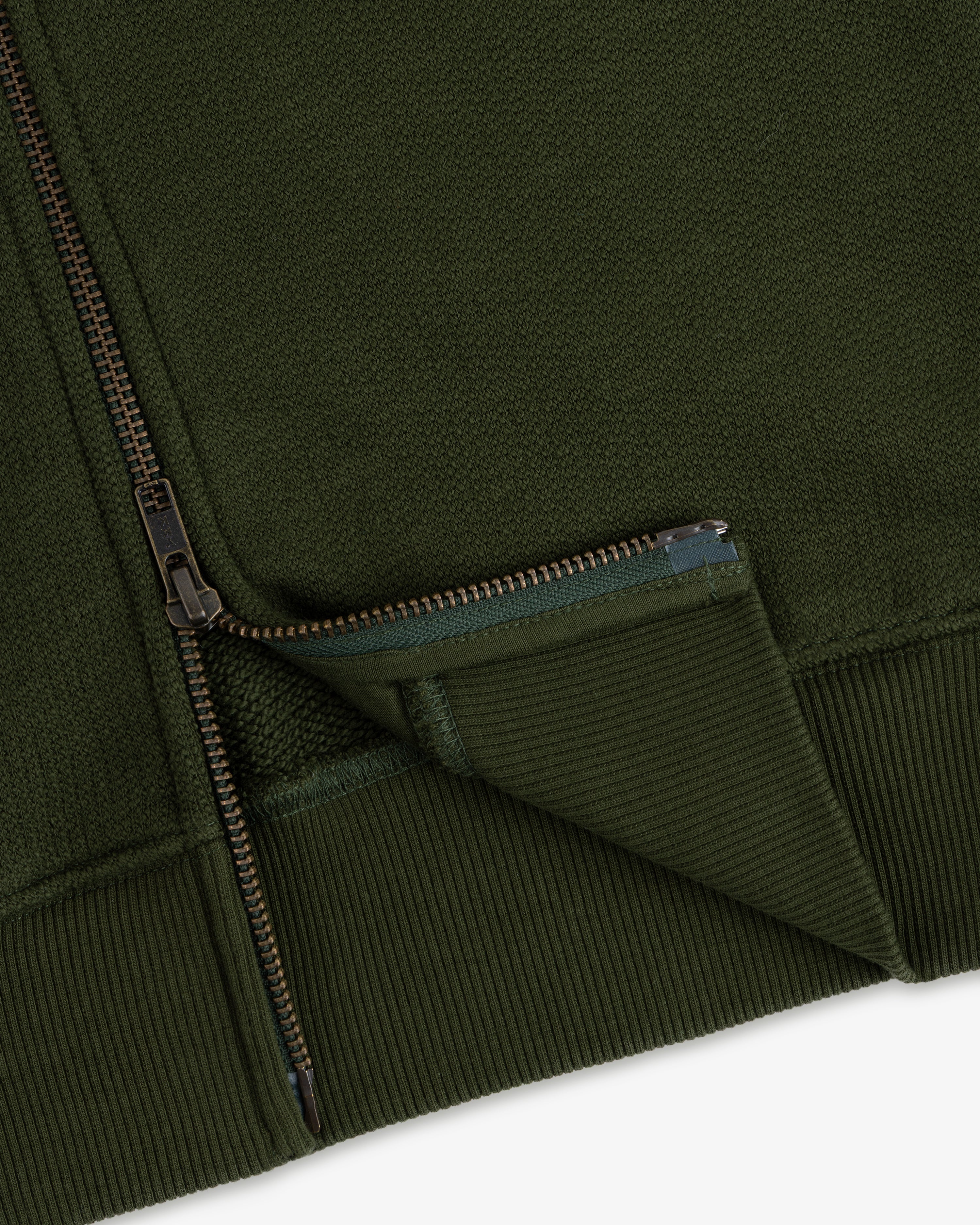 Close-up of the Saint George Track Jacket, highlighting its green fabric, zipper, ribbed cuff, and textured details.