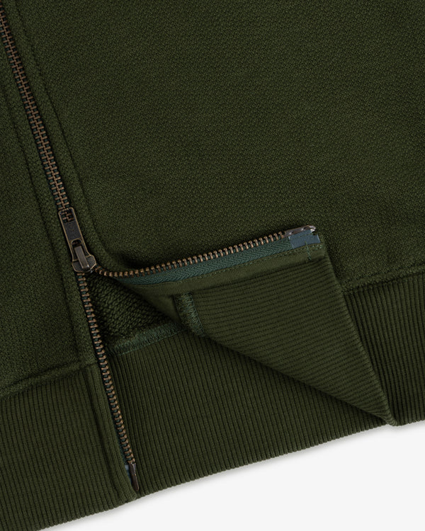 Close-up of the Saint George Track Jacket, highlighting its green fabric, zipper, ribbed cuff, and textured details.