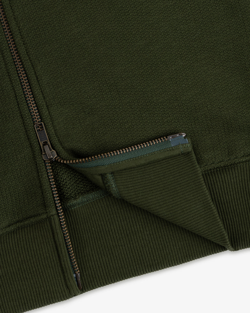 Close-up of the Saint George Track Jacket, highlighting its green fabric, zipper, ribbed cuff, and textured details.