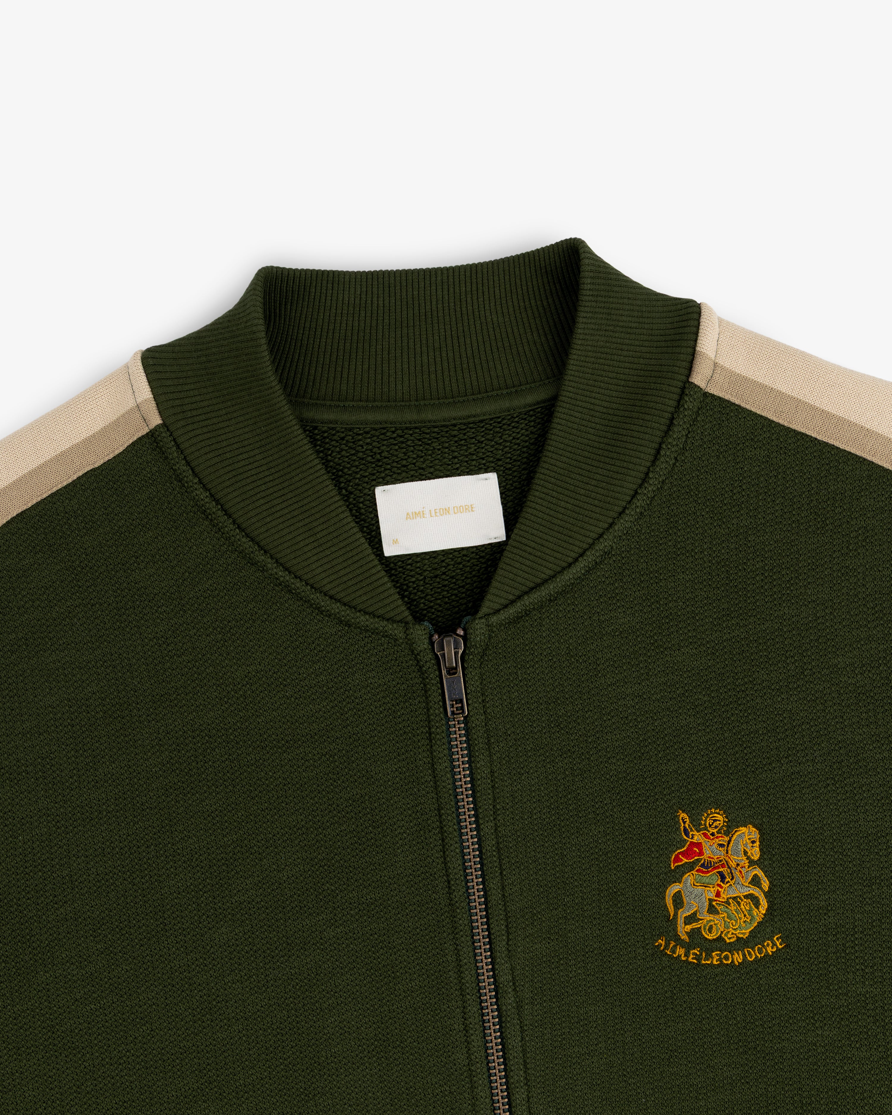 Saint George Track Jacket: Green zip-up with beige shoulder stripes & lion/AIME LEON DORE embroidered emblem.