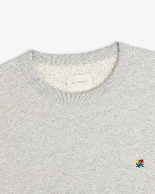 Grey Crest Crewneck Sweatshirt featuring a small embroidered flower motif and an interior neck label.