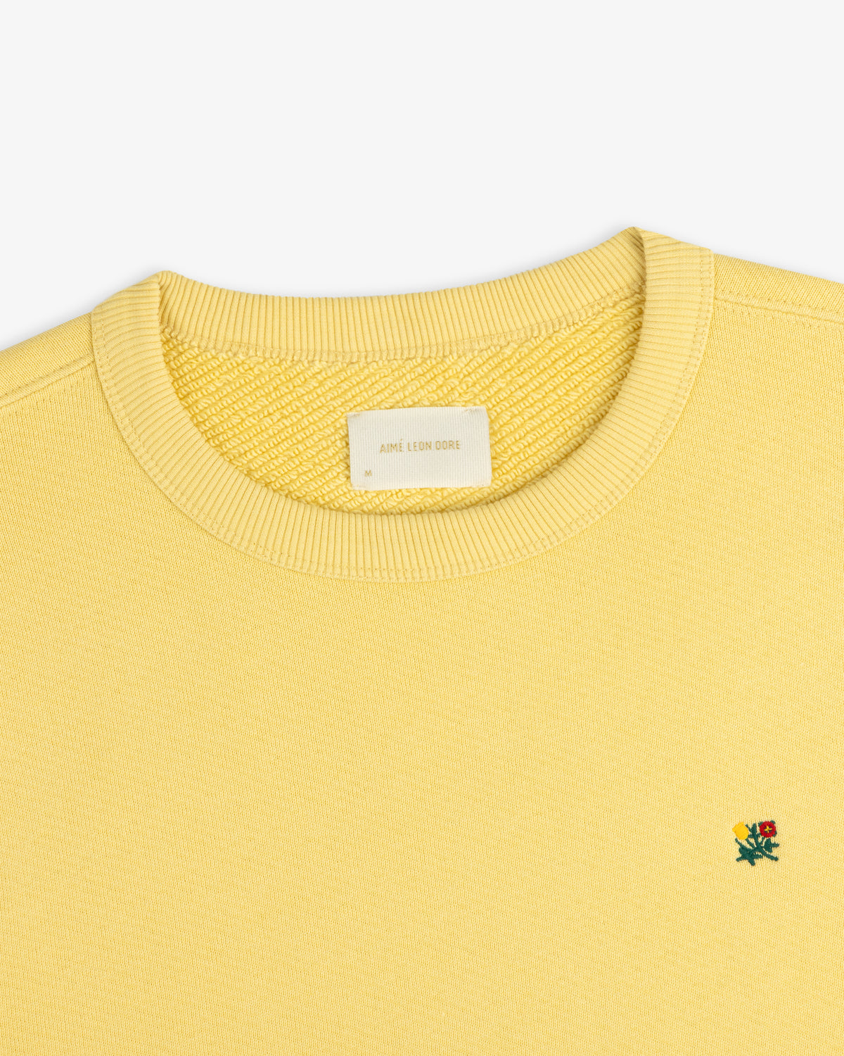 Yellow Crest Crewneck Sweatshirt with a ribbed collar and small flower embroidery on the chest.