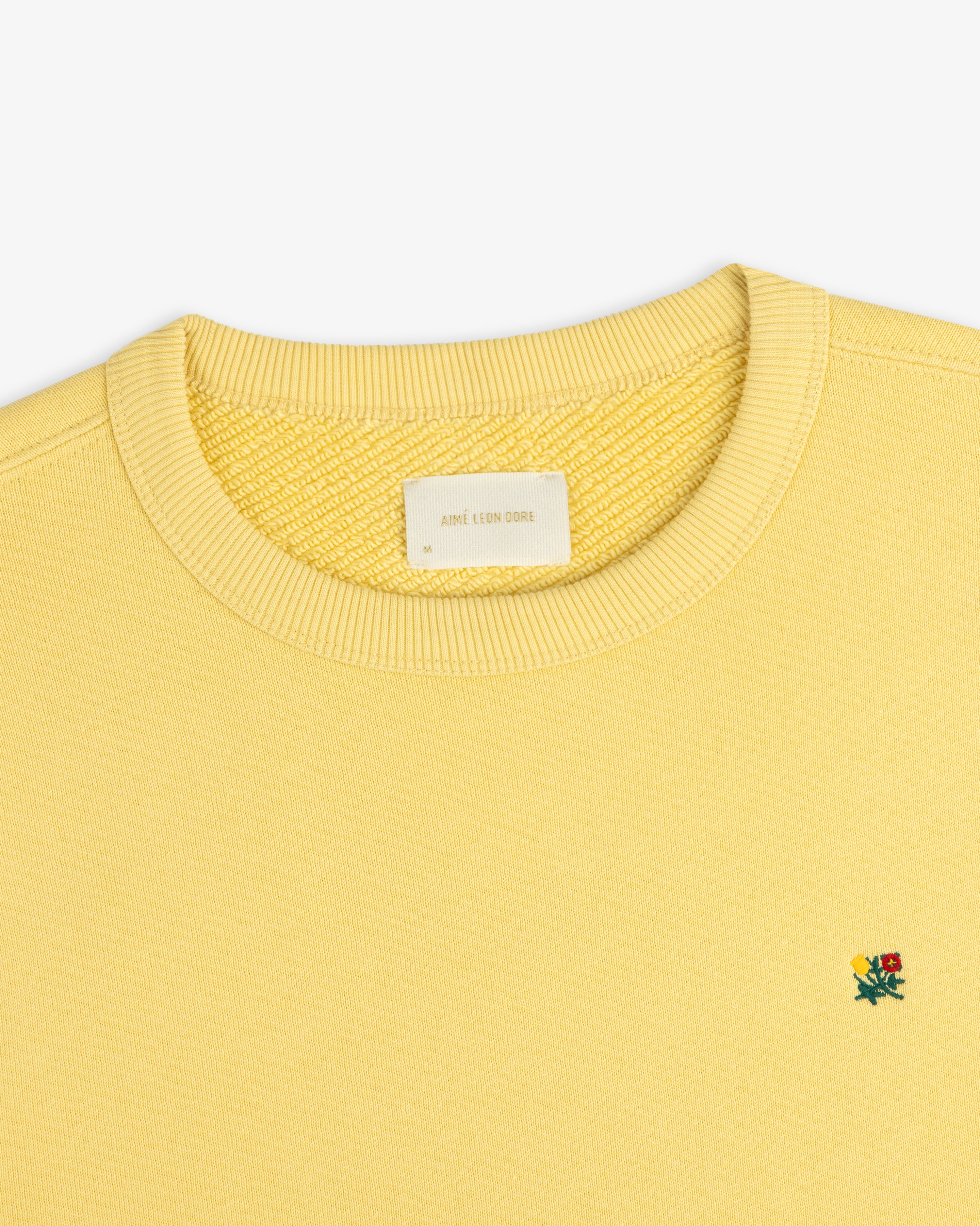 Yellow Crest Crewneck Sweatshirt with a ribbed collar and small flower embroidery on the chest.