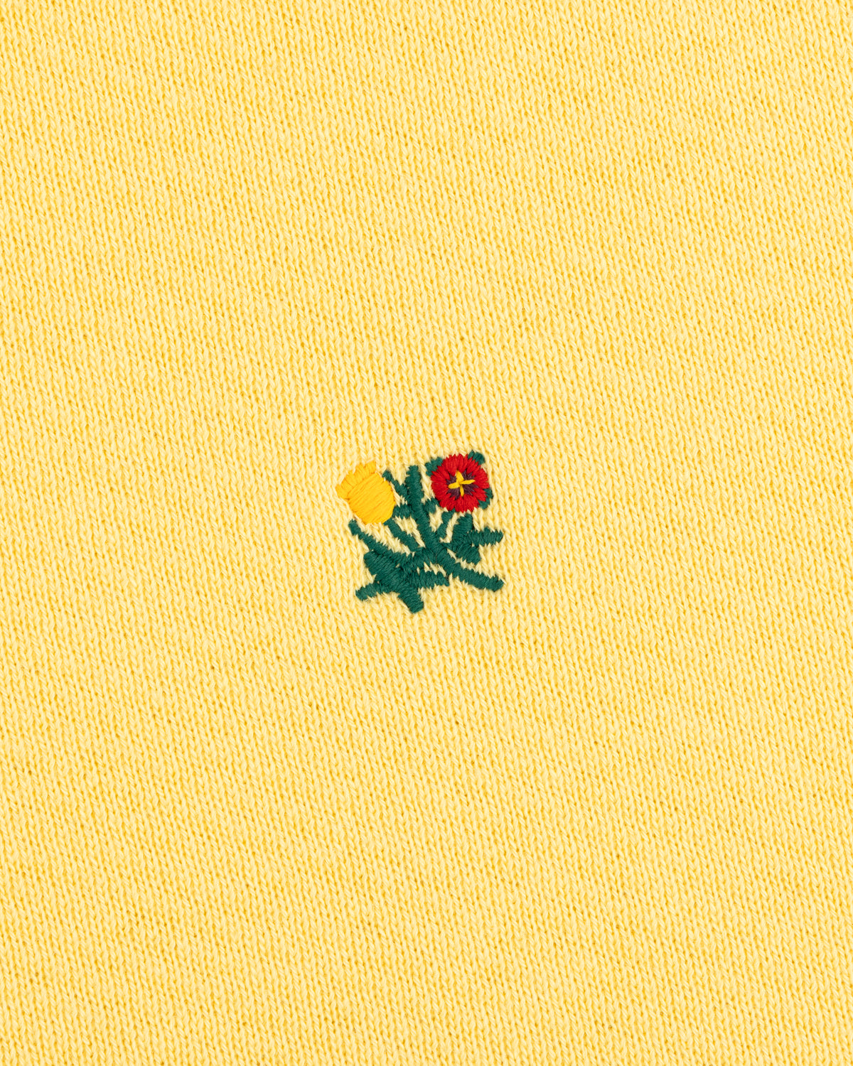 Pale yellow Crest Crewneck Sweatshirt featuring a small embroidered flower design in red, yellow, and green.