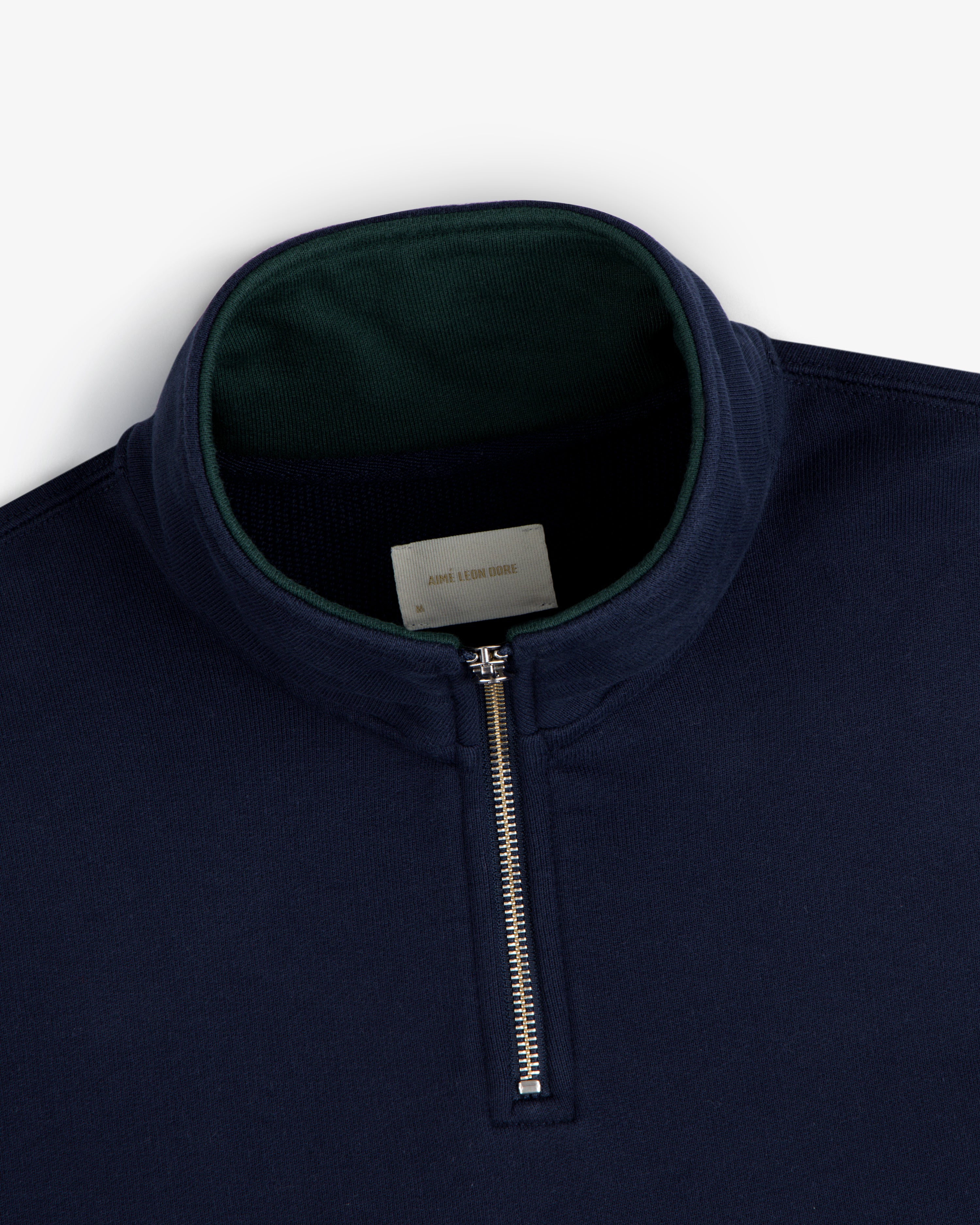 Aimé Souvenir Quarter Zip in navy blue with a silver zipper and green inner collar, displayed on a white background.