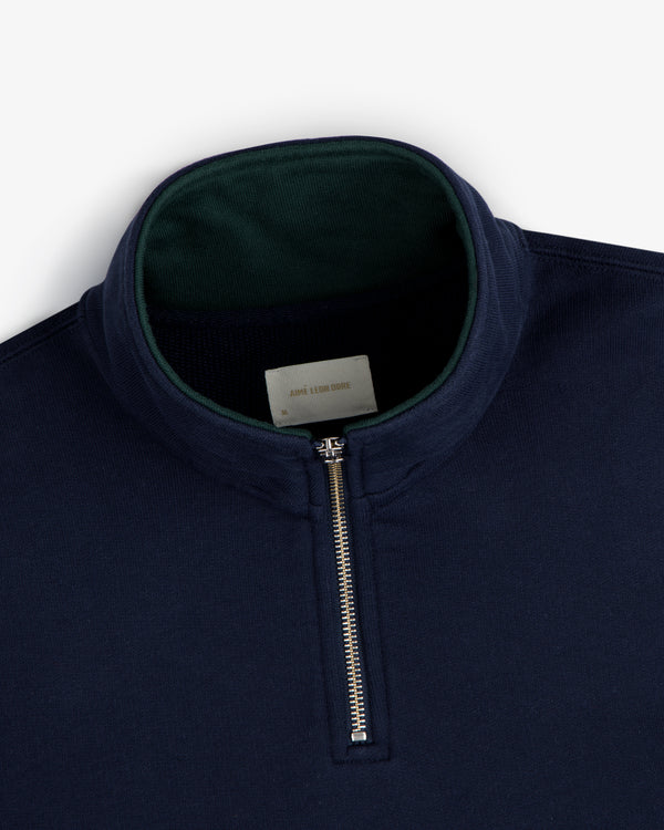 Aimé Souvenir Quarter Zip in navy blue with a silver zipper and green inner collar, displayed on a white background.