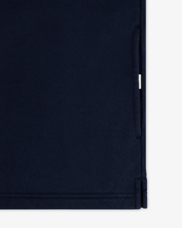 Close-up of the Aimé Souvenir Quarter Zip in navy blue, showing a seam, pocket opening, and small white side tag.