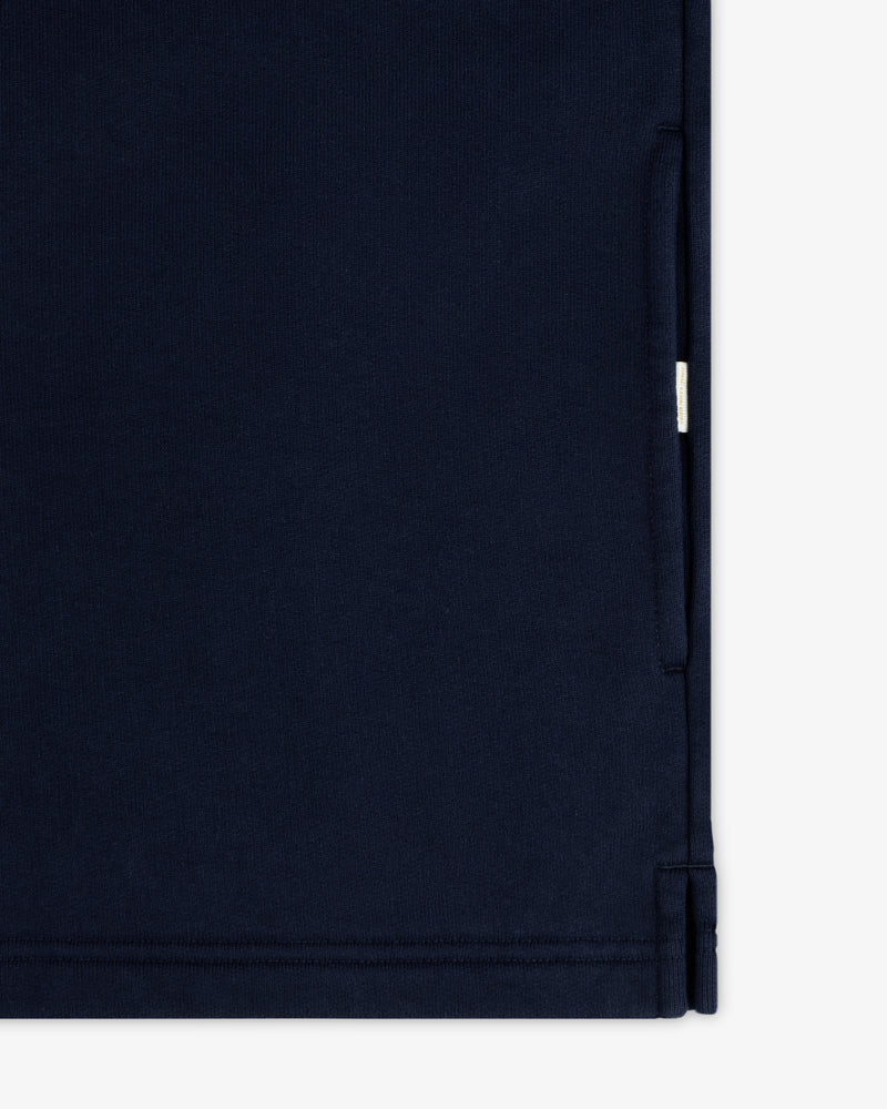 Close-up of the Aimé Souvenir Quarter Zip in navy blue, showing a seam, pocket opening, and small white side tag.