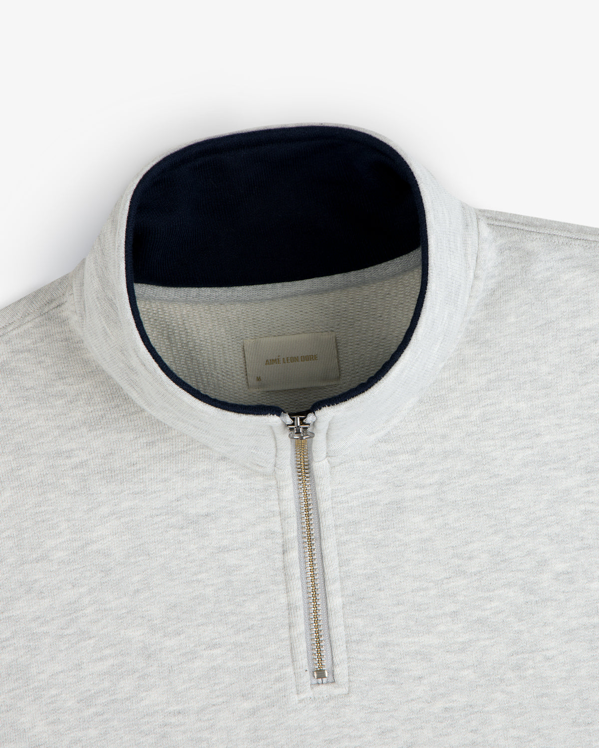 Aimé Souvenir Quarter Zip: light gray pullover with silver zipper and dark navy collar lining.