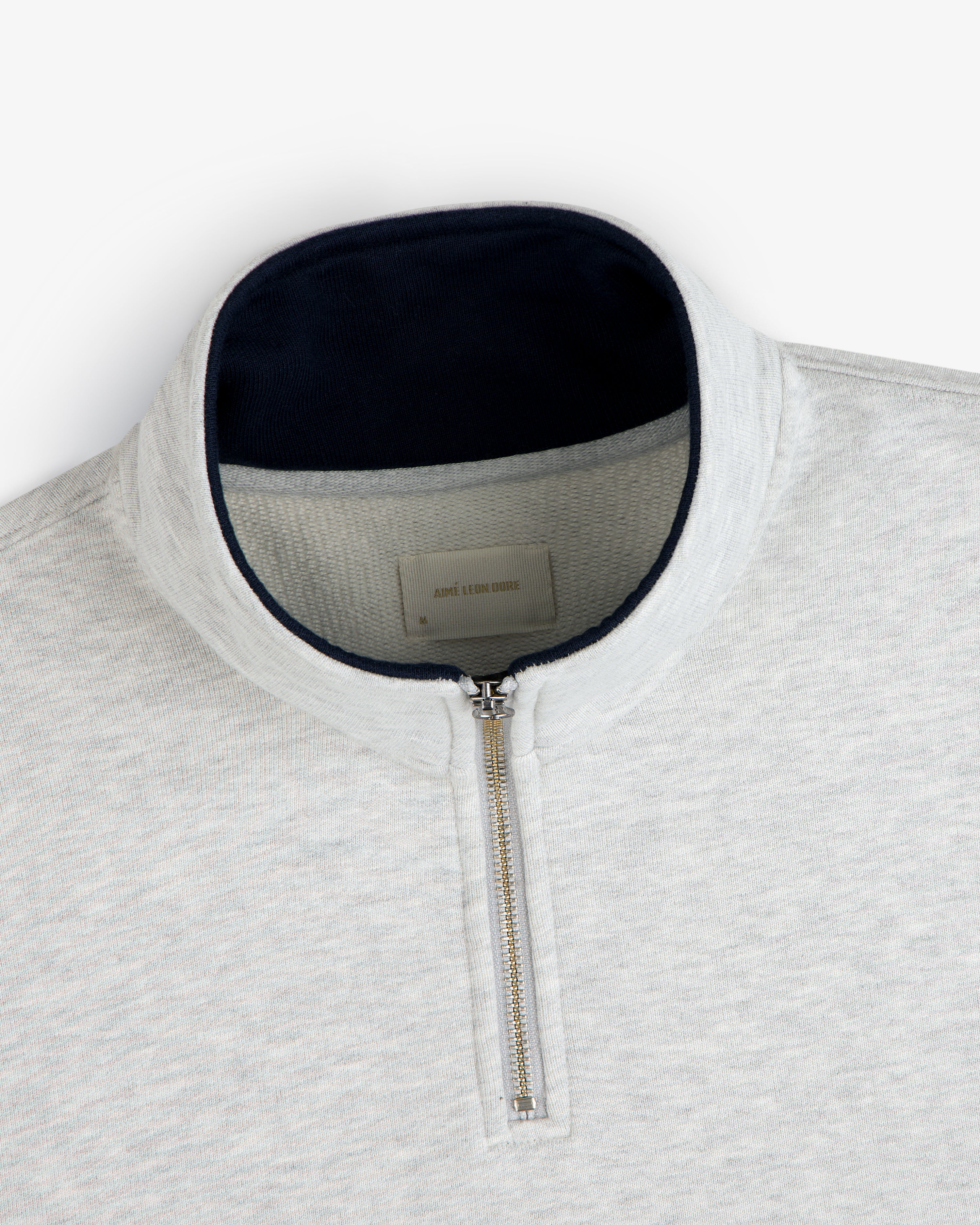 Aimé Souvenir Quarter Zip: light gray pullover with silver zipper and dark navy collar lining.