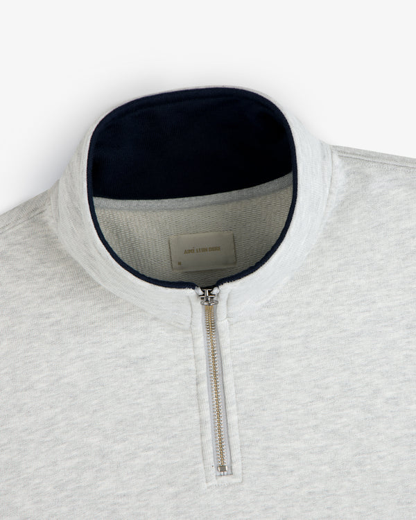 Aimé Souvenir Quarter Zip: light gray pullover with silver zipper and dark navy collar lining.