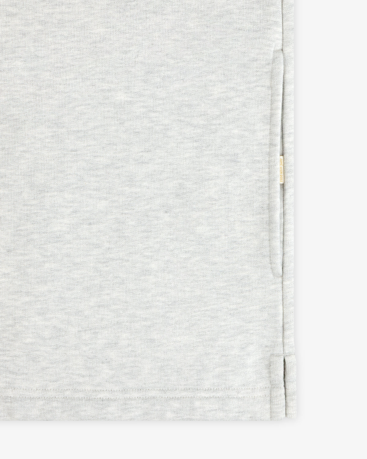 Aimé Souvenir Quarter Zip in light gray fabric with subtle texture, side slit, and beige tag on seam, shown close up.