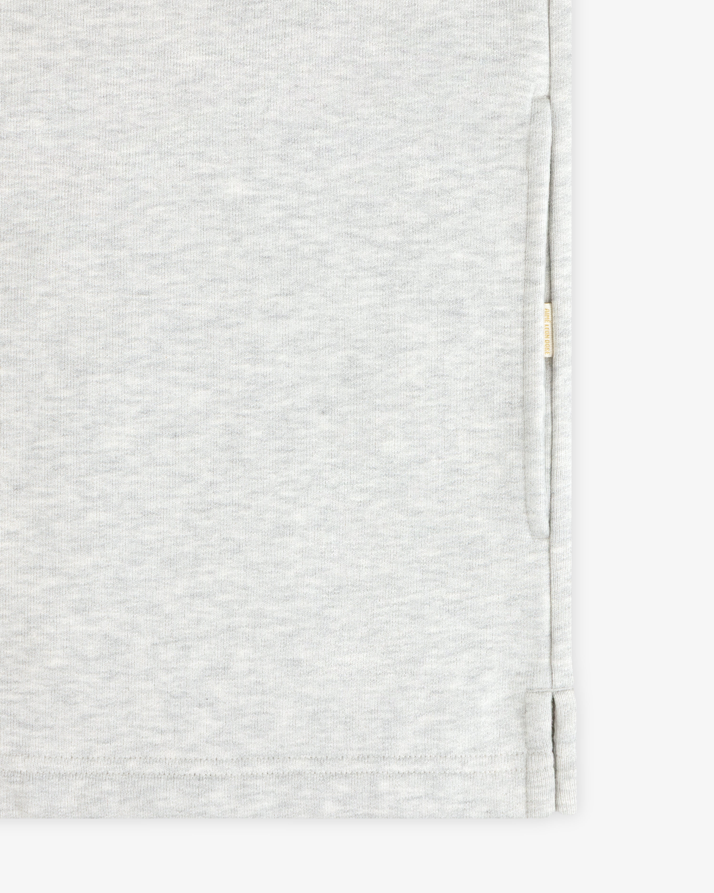Aimé Souvenir Quarter Zip in light gray fabric with subtle texture, side slit, and beige tag on seam, shown close up.