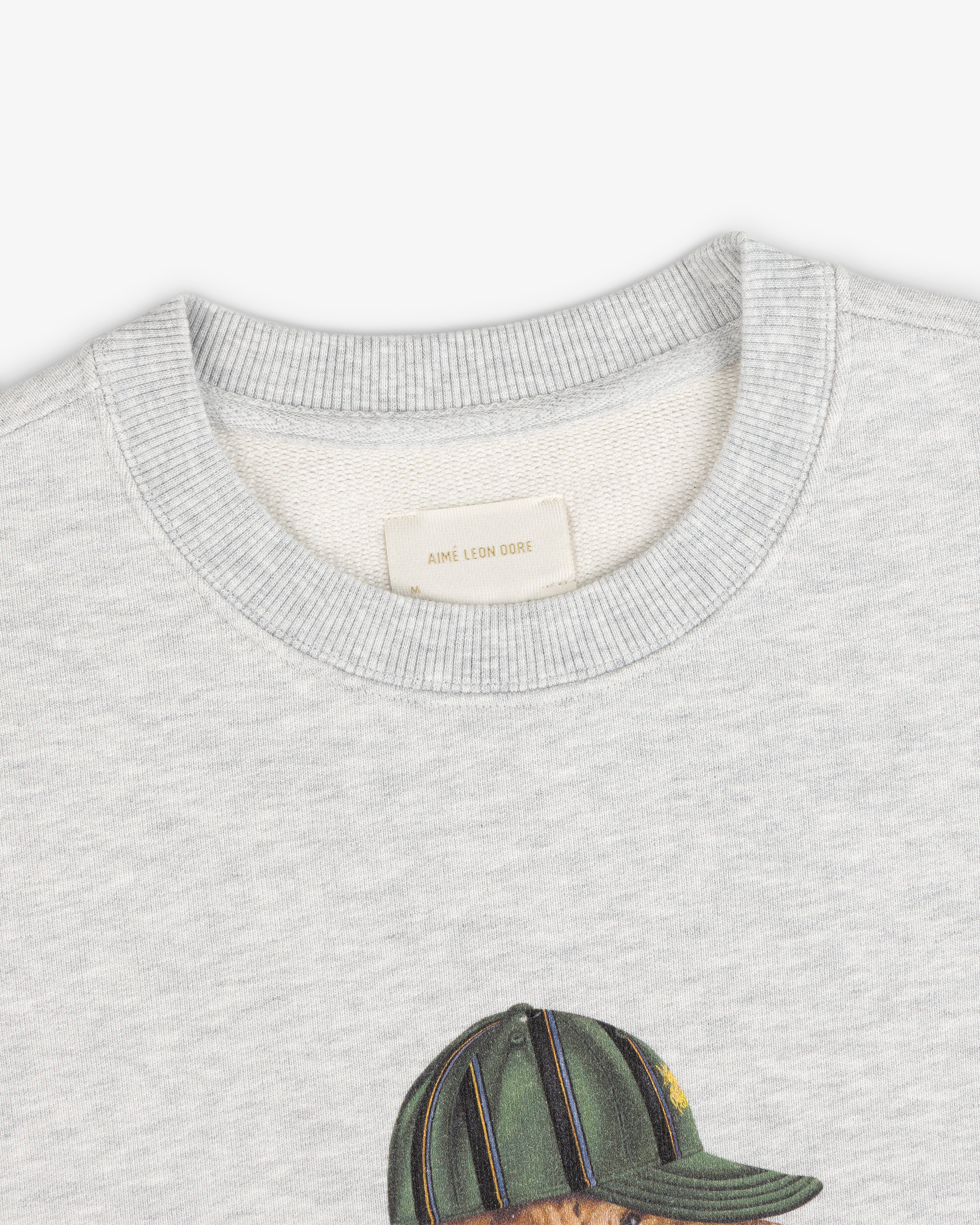 Buddy Crewneck Sweatshirt in light gray with neck tag and top of printed green cap design visible.