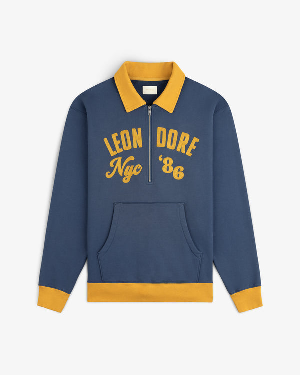 Chainstitch ’86 Half Zip Pullover in navy blue with a yellow collar, cuffs, hem, and gold embroidered chest text.