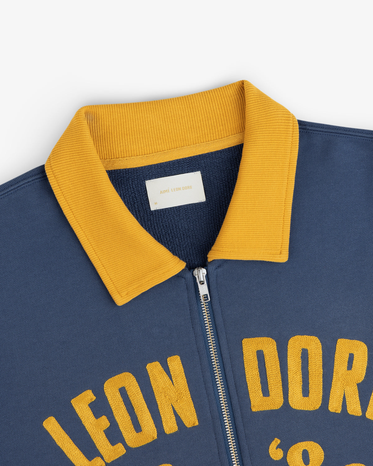 Chainstitch ’86 Half Zip Pullover in navy blue with a gold ribbed collar and yellow chainstitched lettering.