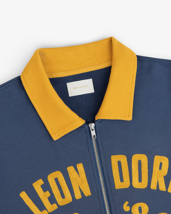 Chainstitch ’86 Half Zip Pullover in navy blue with a gold ribbed collar and yellow chainstitched lettering.