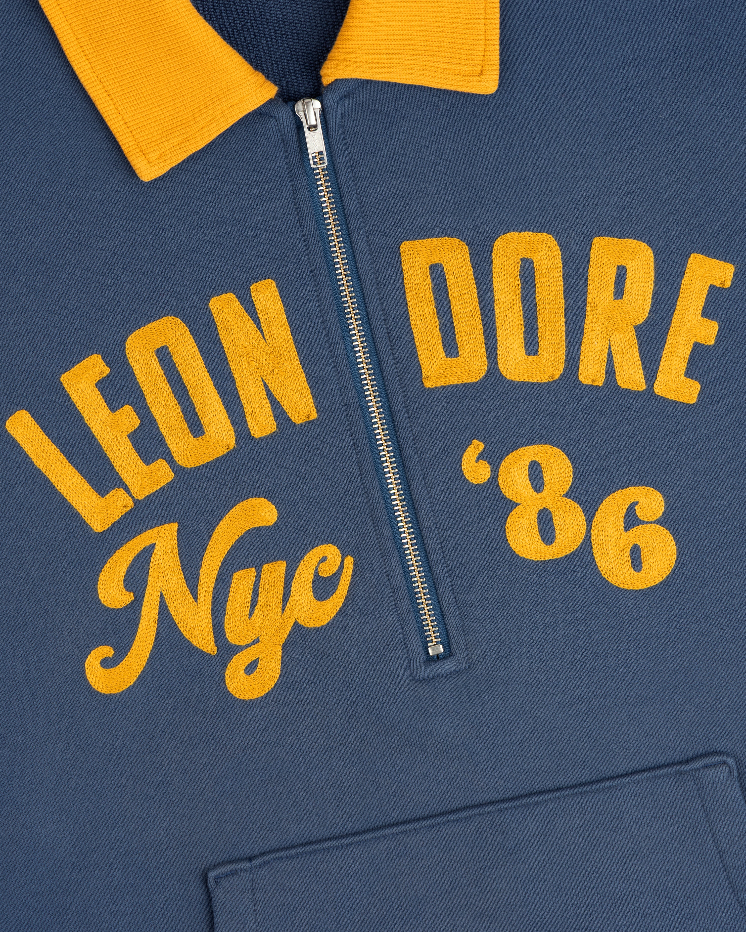 Chainstitch ’86 Half Zip Pullover in blue with a yellow collar and yellow embroidered text reading Leon Dore Nyc 86.
