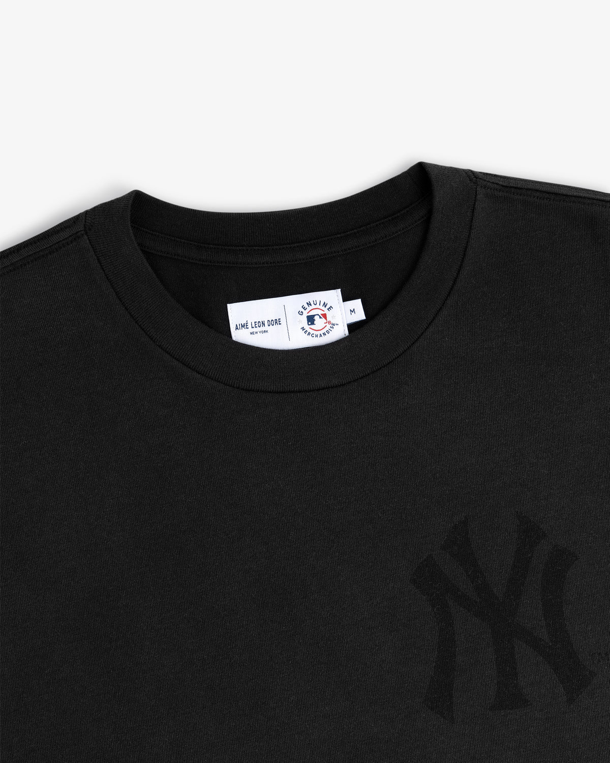 Close-up of a Yankees Washed Logo Tee in black with a subtle logo and neck tag displaying size M.