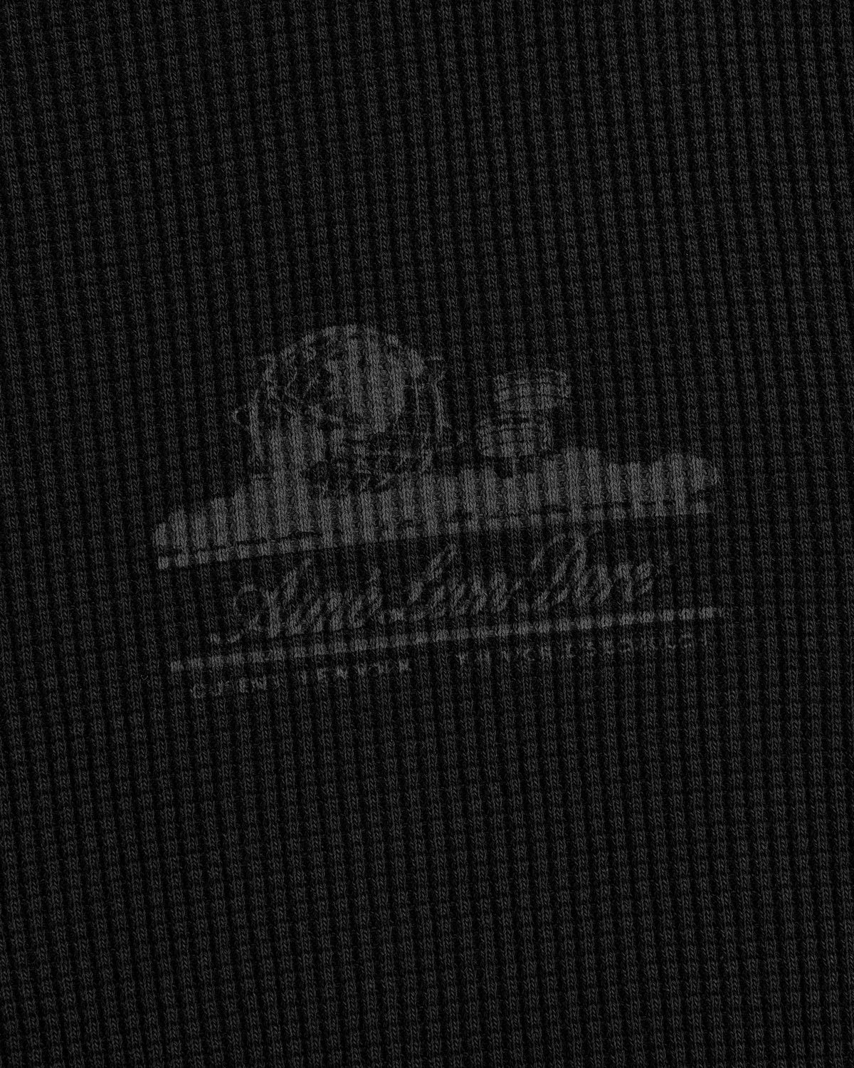 A faded white Unisphere logo on textured dark gray fabric of the Long-Sleeve Unisphere Waffle Thermal.