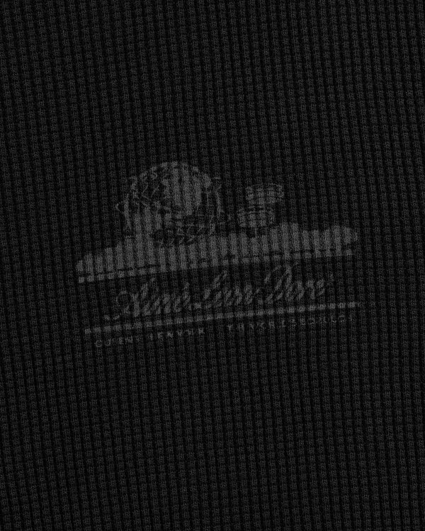 A faded white Unisphere logo on textured dark gray fabric of the Long-Sleeve Unisphere Waffle Thermal.