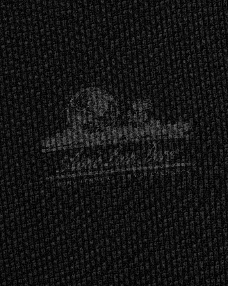 A faded white Unisphere logo on textured dark gray fabric of the Long-Sleeve Unisphere Waffle Thermal.